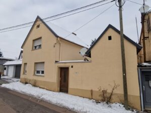 Haus mit Schneebedecktem Dach und Stromleitungen in einer winterlichen Umgebung.